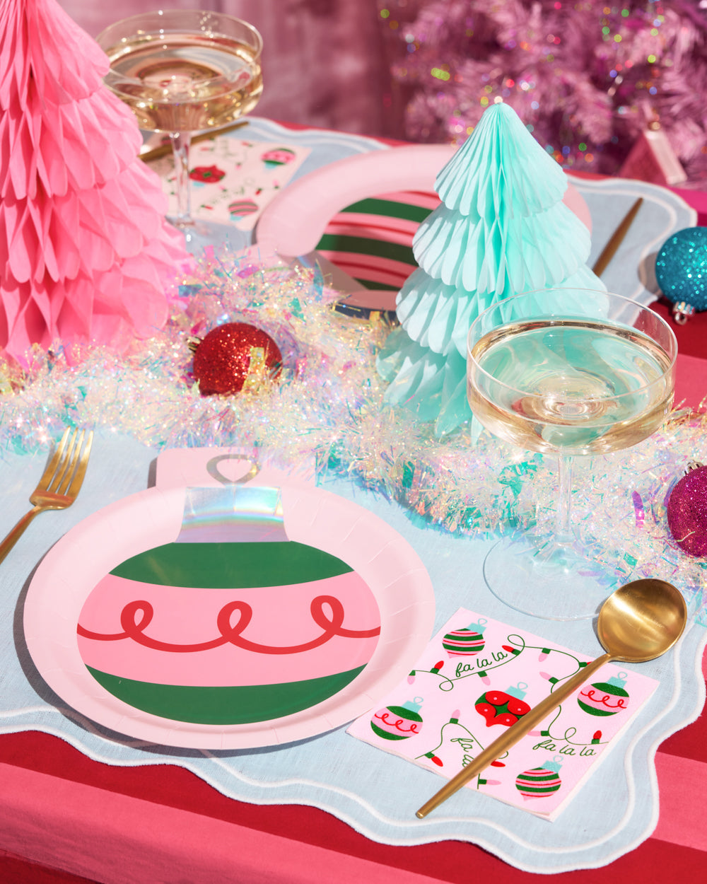 Decorative table setting with Christmas ornaments, glasses, and a pink tree.