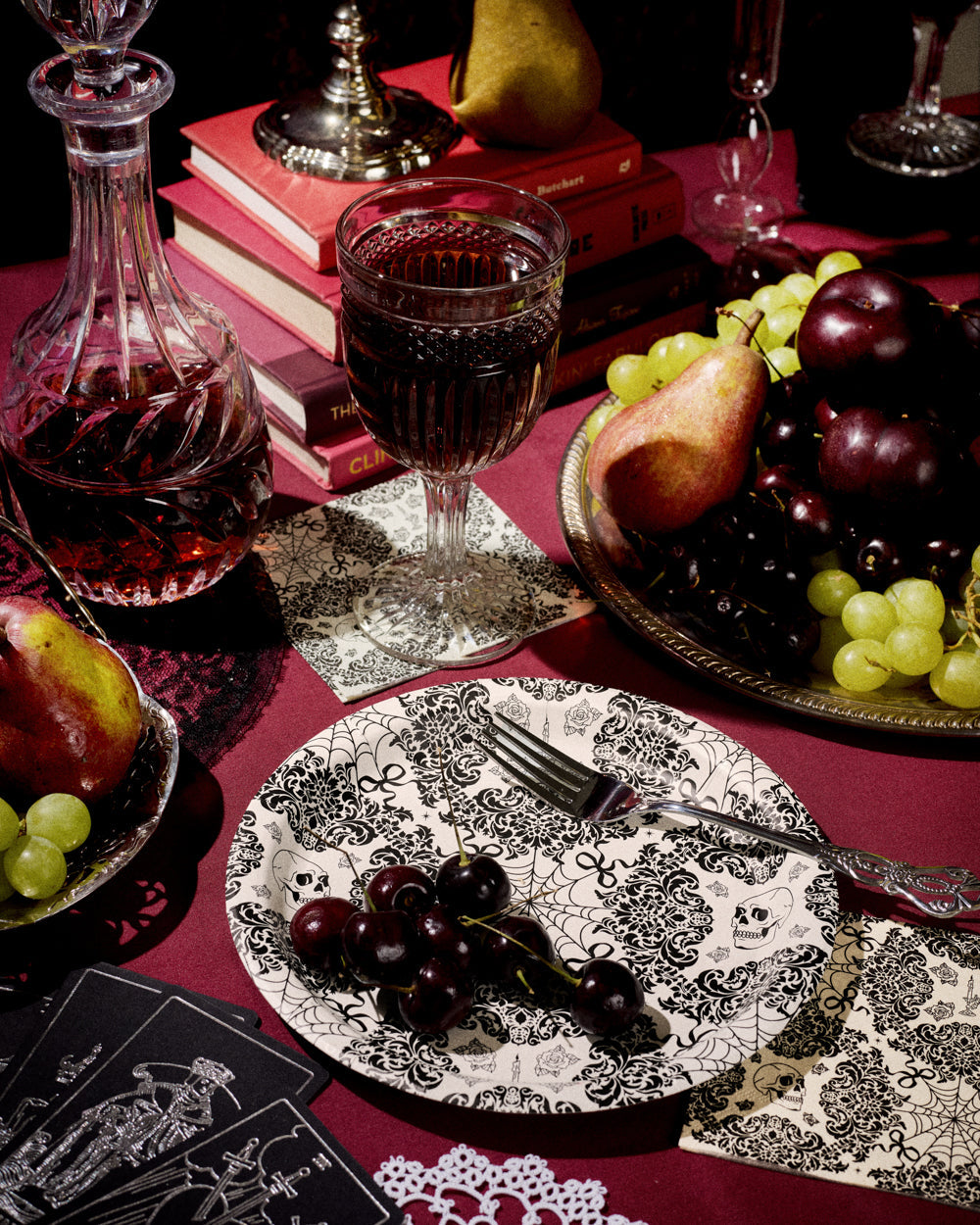 Table setting with wine, fruit, and decorative elements on a red tablecloth.