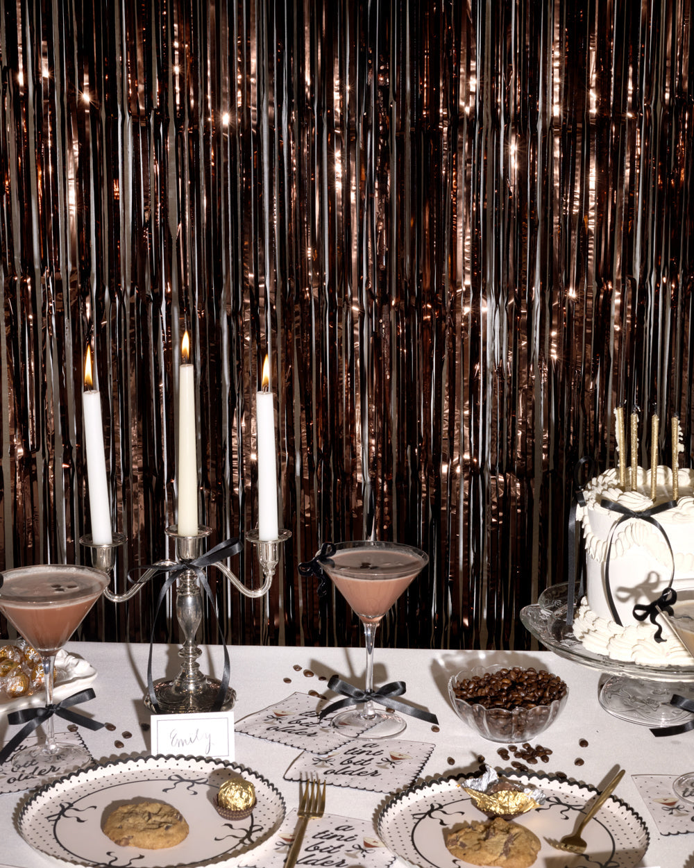 Decorative table setting with candles, cake, and cocktails against a metallic curtain backdrop.