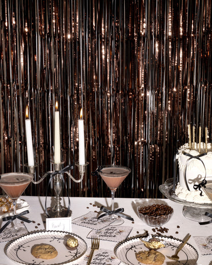 Decorative table setting with candles, cake, and cocktails against a metallic curtain backdrop.