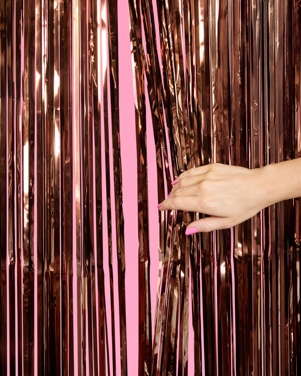 Hand reaching towards a rose gold tinsel curtain