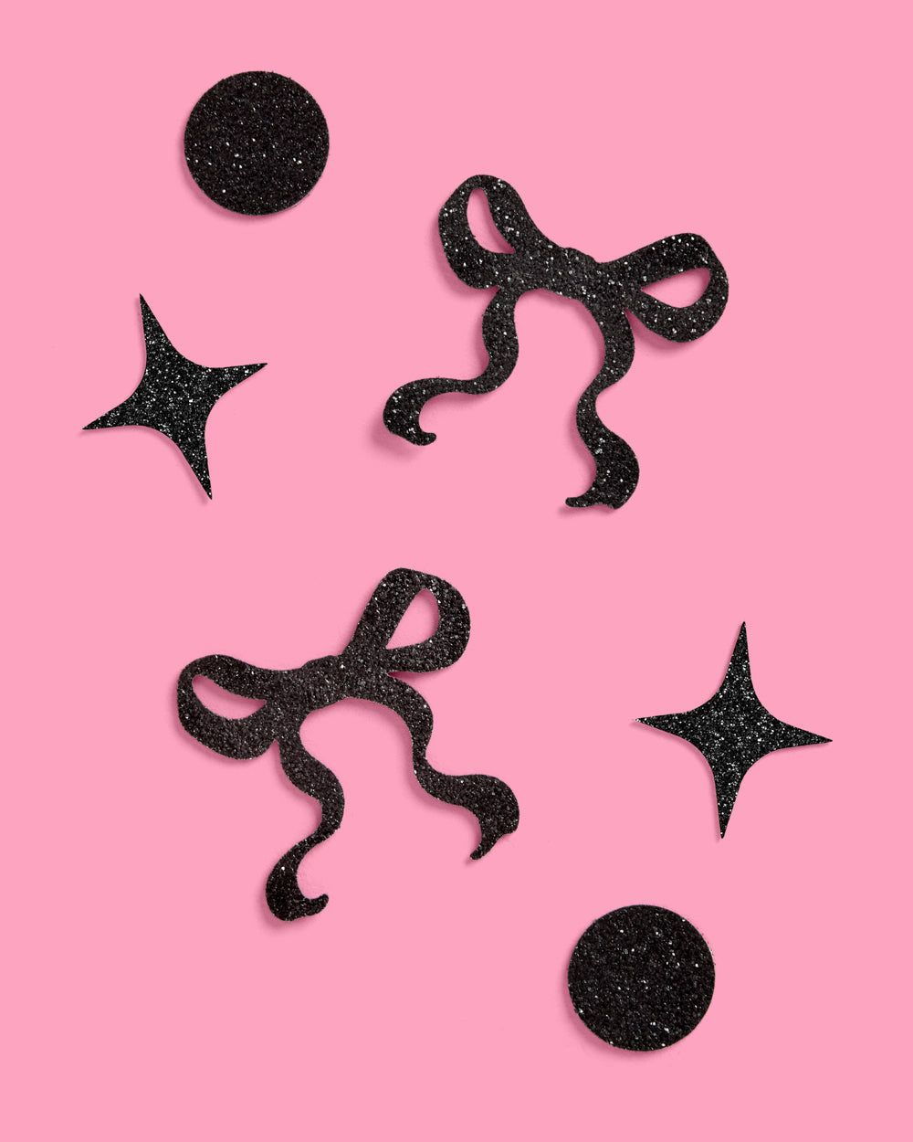 Black glittery star and bow shapes on a pink background