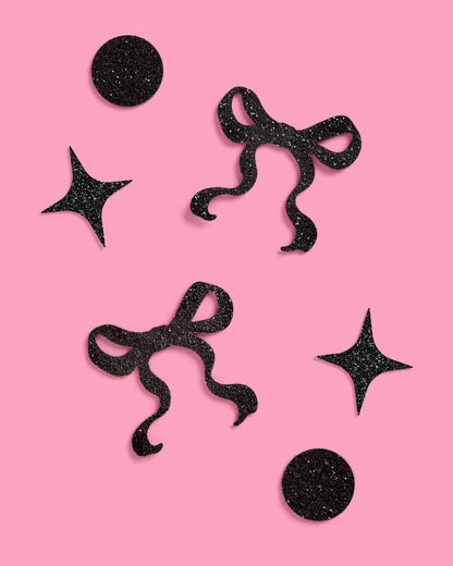 Black glittery star and bow shapes on a pink background