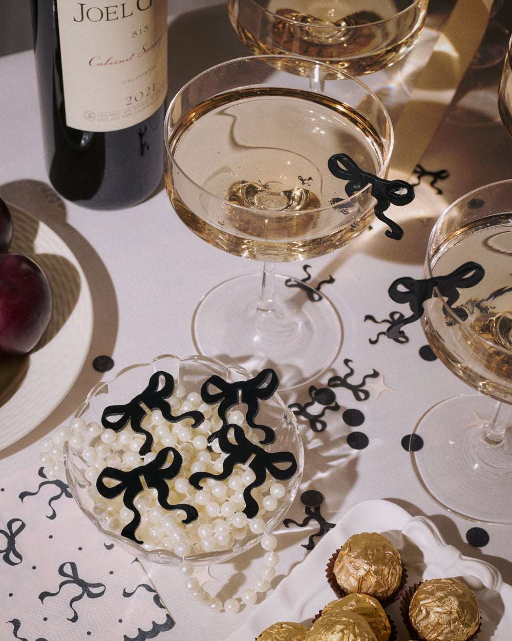 Two glasses of white wine on a table with decorative black bows and gold chocolates.