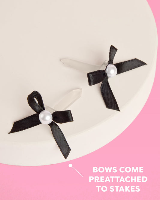 Two black bows with pearls on a pink and white background