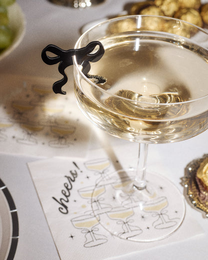 Wine glass with a decorative black bow on a table setting with a 'cheers' card.