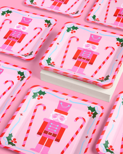 Set of Christmas-themed paper plates with nutcracker design on a pink background