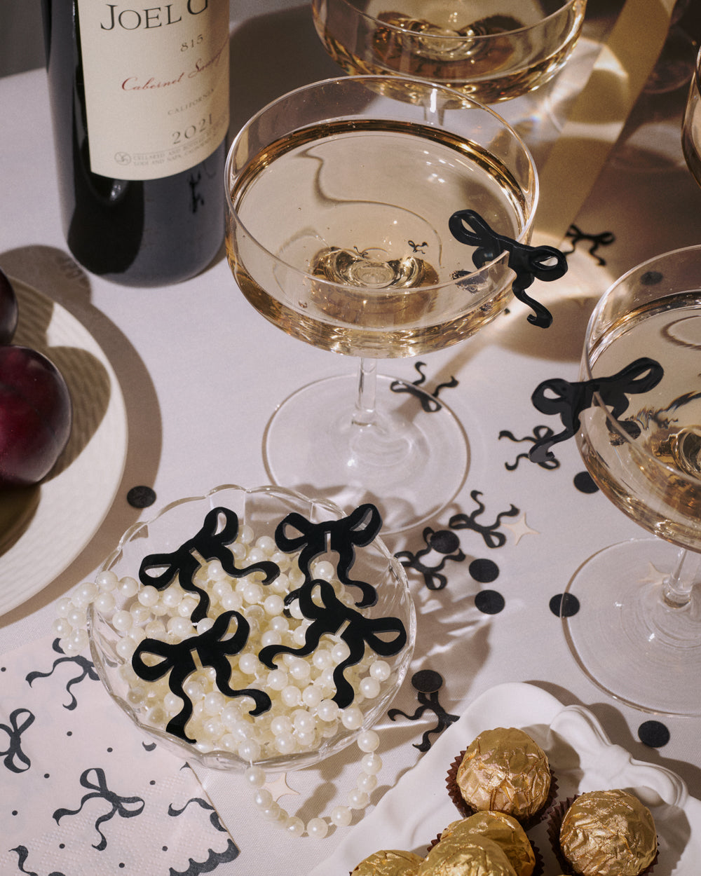 Two glasses of white wine on a table with decorative black bows and gold chocolates.