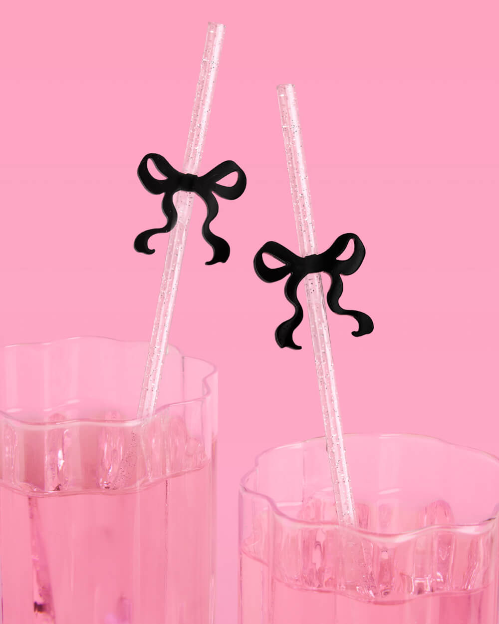 Clear plastic straws with black bow-shaped ends in front of a pink background