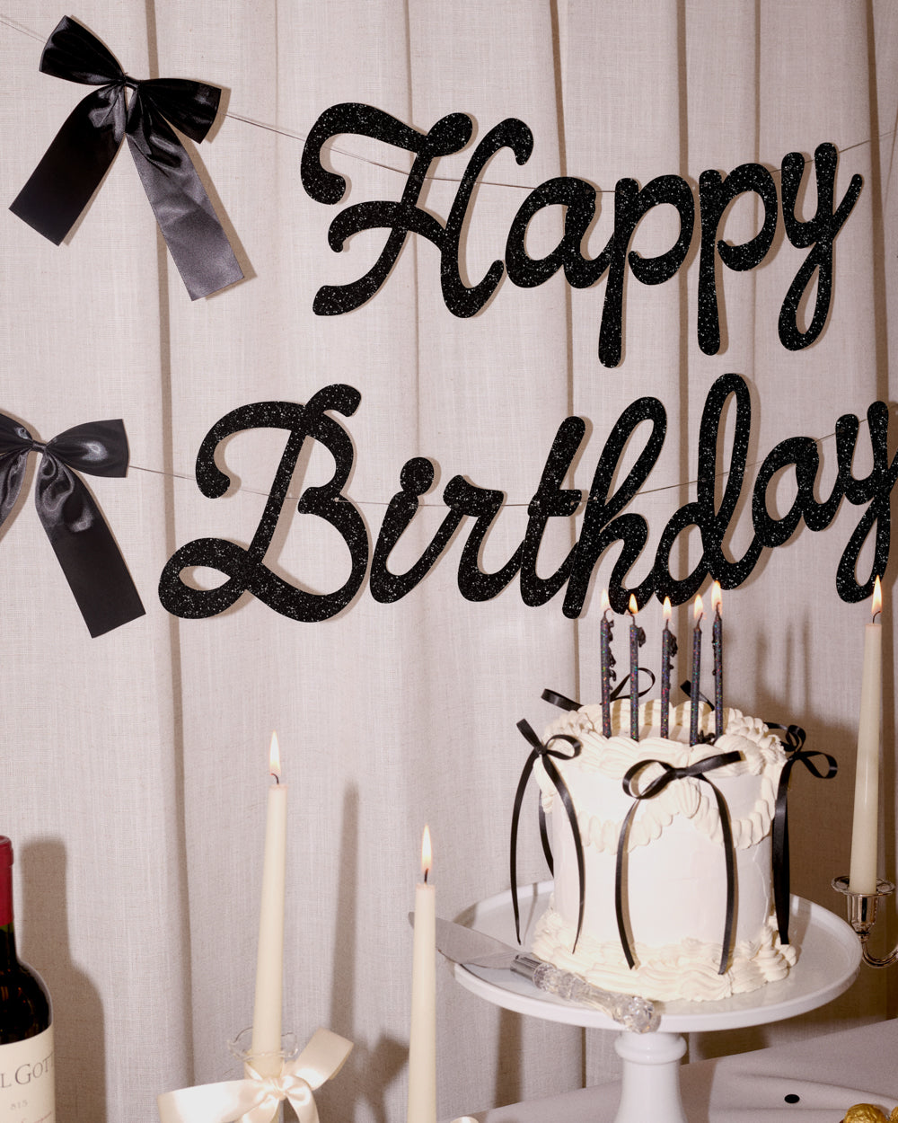Black 'Happy Birthday' sign with decorative ribbons and a cake in the background.