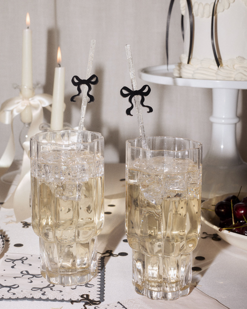 Two crystal glasses with white liquid on a decorative table setting with candles and a cake stand.