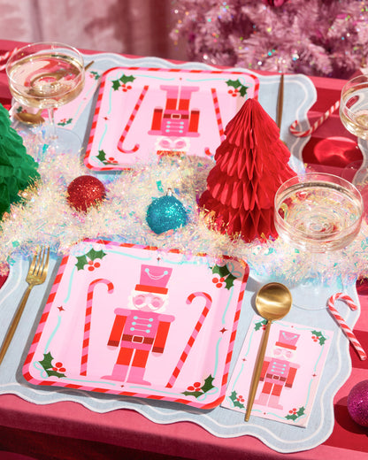 Christmas-themed table setting with decorative plates, glasses, and ornaments on a red tablecloth.