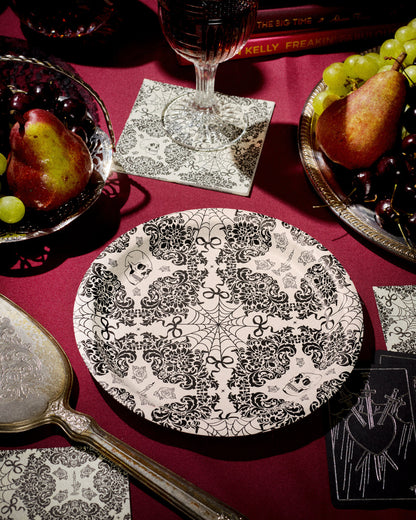 Decorative black and white plate on a red tablecloth with fruit and glasses.