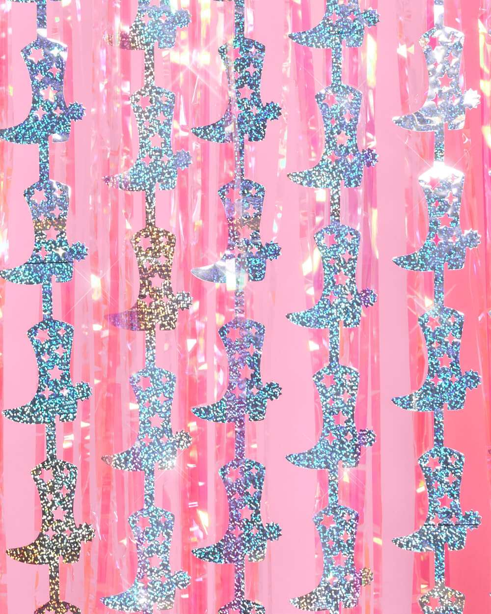 Silver glitter cowgirl boot cutouts hanging in rows over a pink plastic fringe curtain.