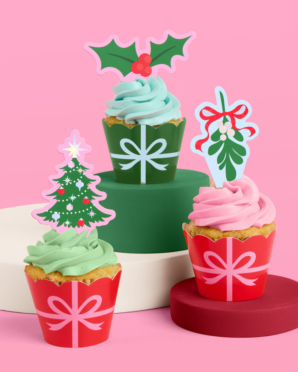 Three cupcakes with festive decorations on a pink background