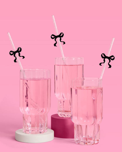 Three glasses of pink liquid with straws and black ribbon decorations on a pink background