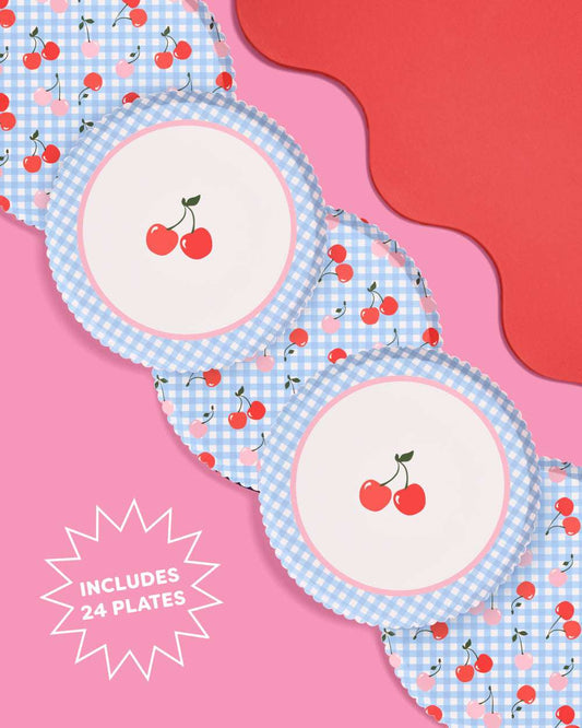 Five round paper plates with blue gingham and cherry patterns on a pink background. Text reads includes 24 plates.