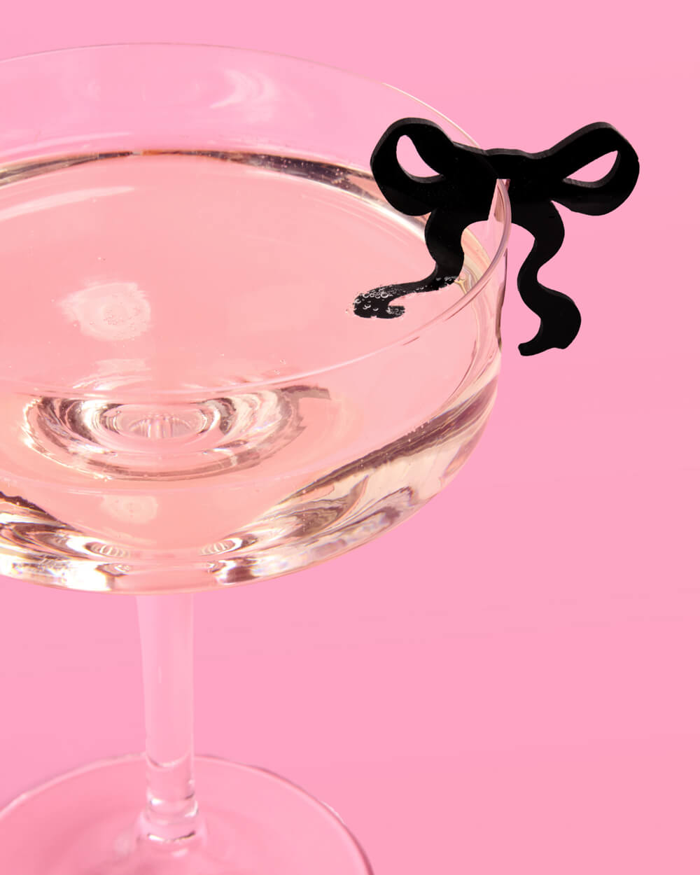 Cocktail glass with a black bow-shaped drink marker on a pink background