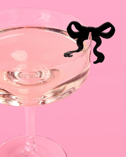 Cocktail glass with a black bow-shaped drink marker on a pink background
