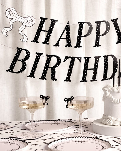 Decorative 'Happy Birthday' banner with a table setting featuring glasses and a cake.