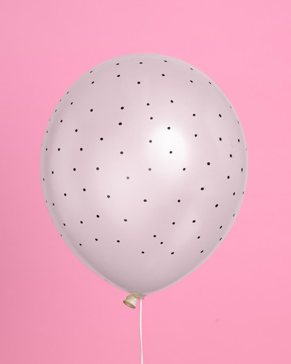 White balloon with black dots on a pink background