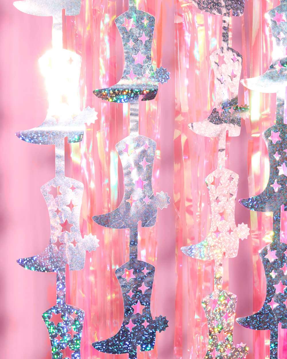 Pink iridescent cowgirl boot garlands with star cutouts layered over a shiny pink plastic fringe curtain.