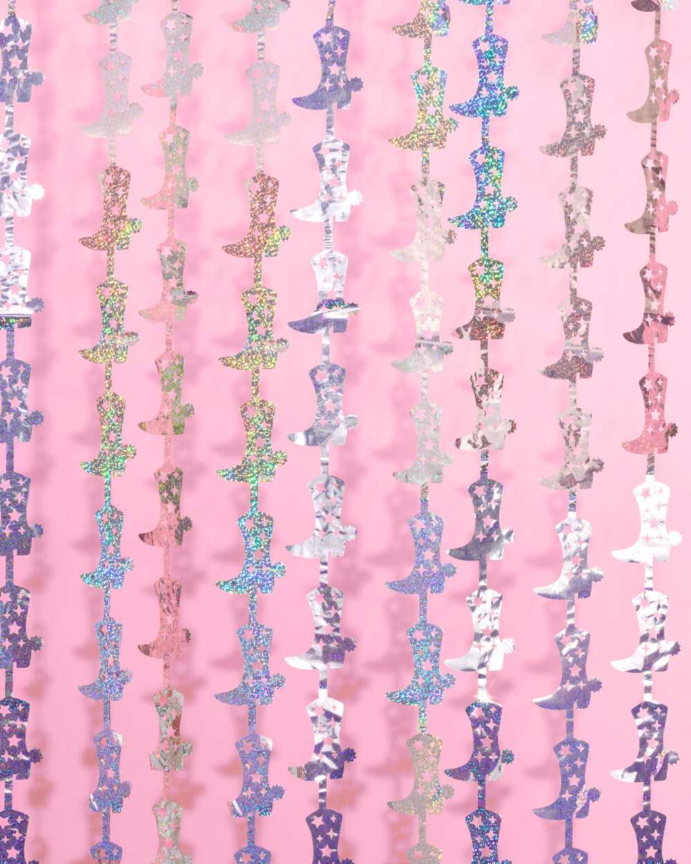 Holographic silver cowgirl boot shaped fringe curtains hanging in vertical rows against a pink background.