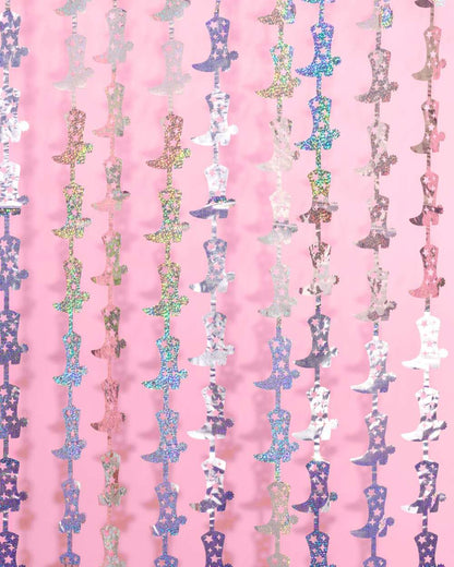 Holographic silver cowgirl boot shaped fringe curtains hanging in vertical rows against a pink background.
