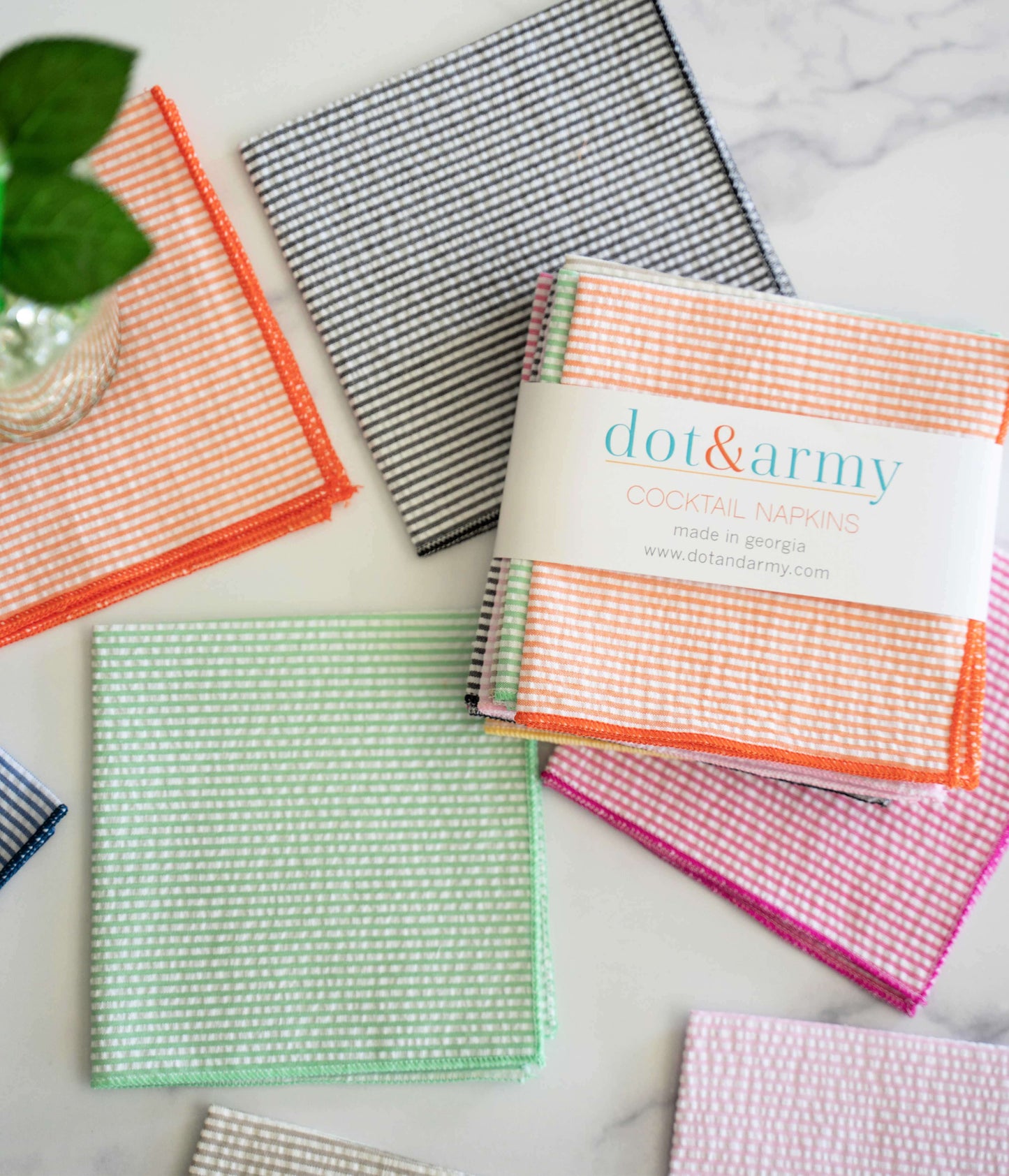Eight colorful seersucker dot&army Cocktail Napkins in a stack and spread out on a white marble surface.