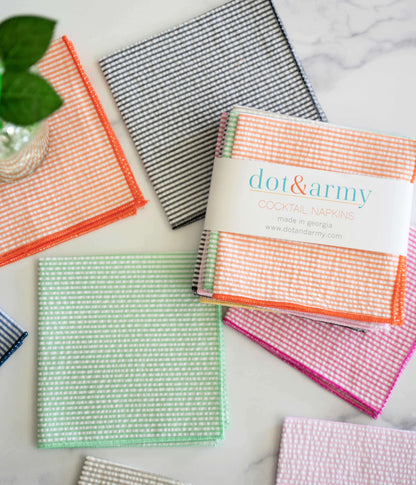 Eight colorful seersucker dot&army Cocktail Napkins in a stack and spread out on a white marble surface.