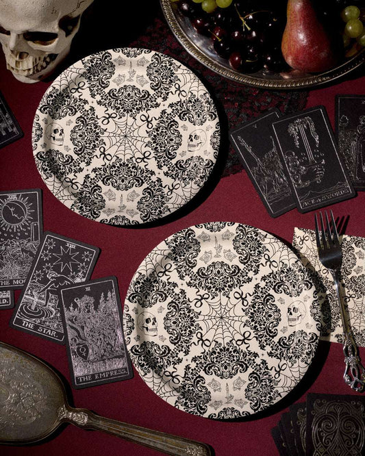 Decorative black and white plates with skull and spider web patterns on a red tablecloth with tarot cards and a skull.
