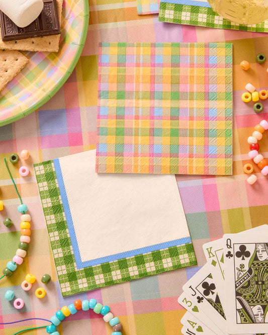 Two square paper napkins with green and multicolored gingham plaid patterns, surrounded by beads and playing cards.