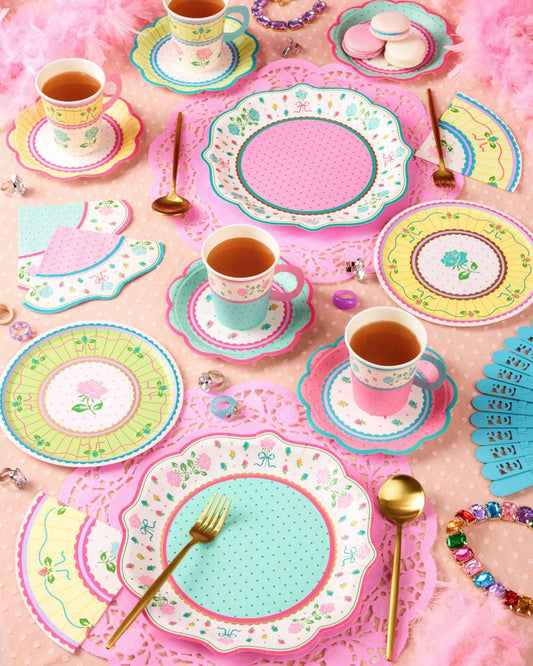 Floral paper plates, cups, and napkins in pink, blue, and yellow arranged with gold cutlery on a pink tablecloth.