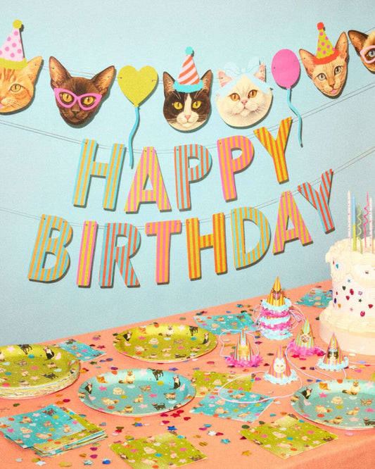 Cat face banner and Happy Birthday sign above a table with cat print plates, napkins, and small party hats.