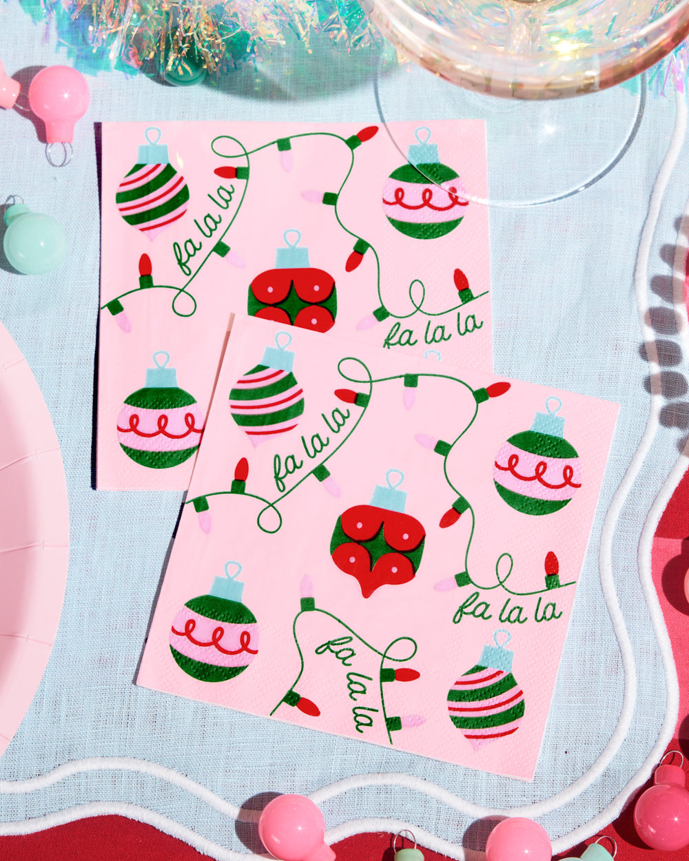 Pink Christmas-themed napkins with ornaments and 'fa la la' text on a decorative surface.
