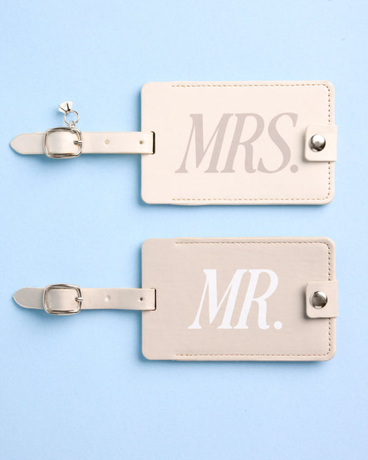Two cream rectangular luggage tags with straps printed with MRS. and MR. in white text on a blue background.