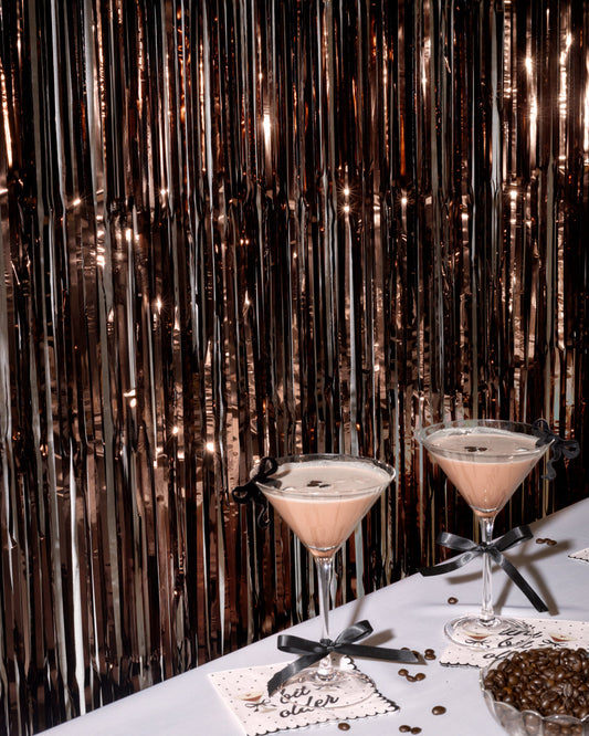 Two cocktails on a table with a festive, metallic curtain background