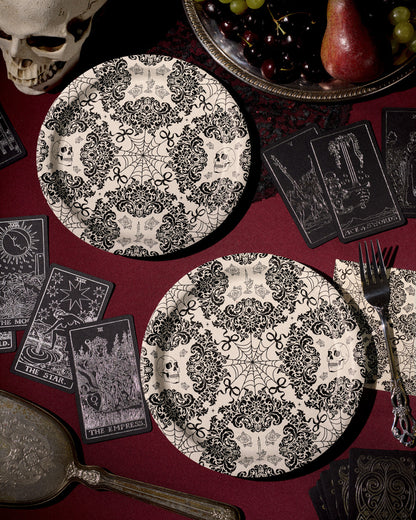 Decorative black and white plates with skull and spider web patterns on a red tablecloth with tarot cards and a skull.