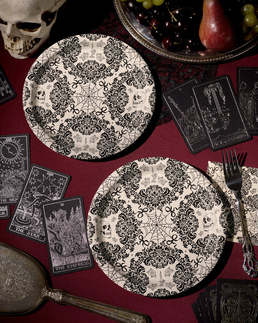 Decorative black and white plates with skull and spider web patterns on a red tablecloth with tarot cards and a skull.