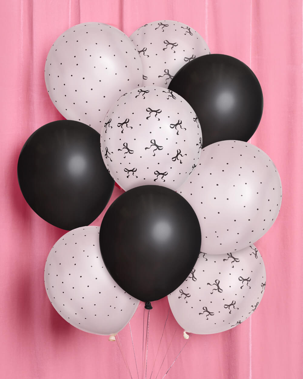 Black and white balloons with bow patterns against a pink background