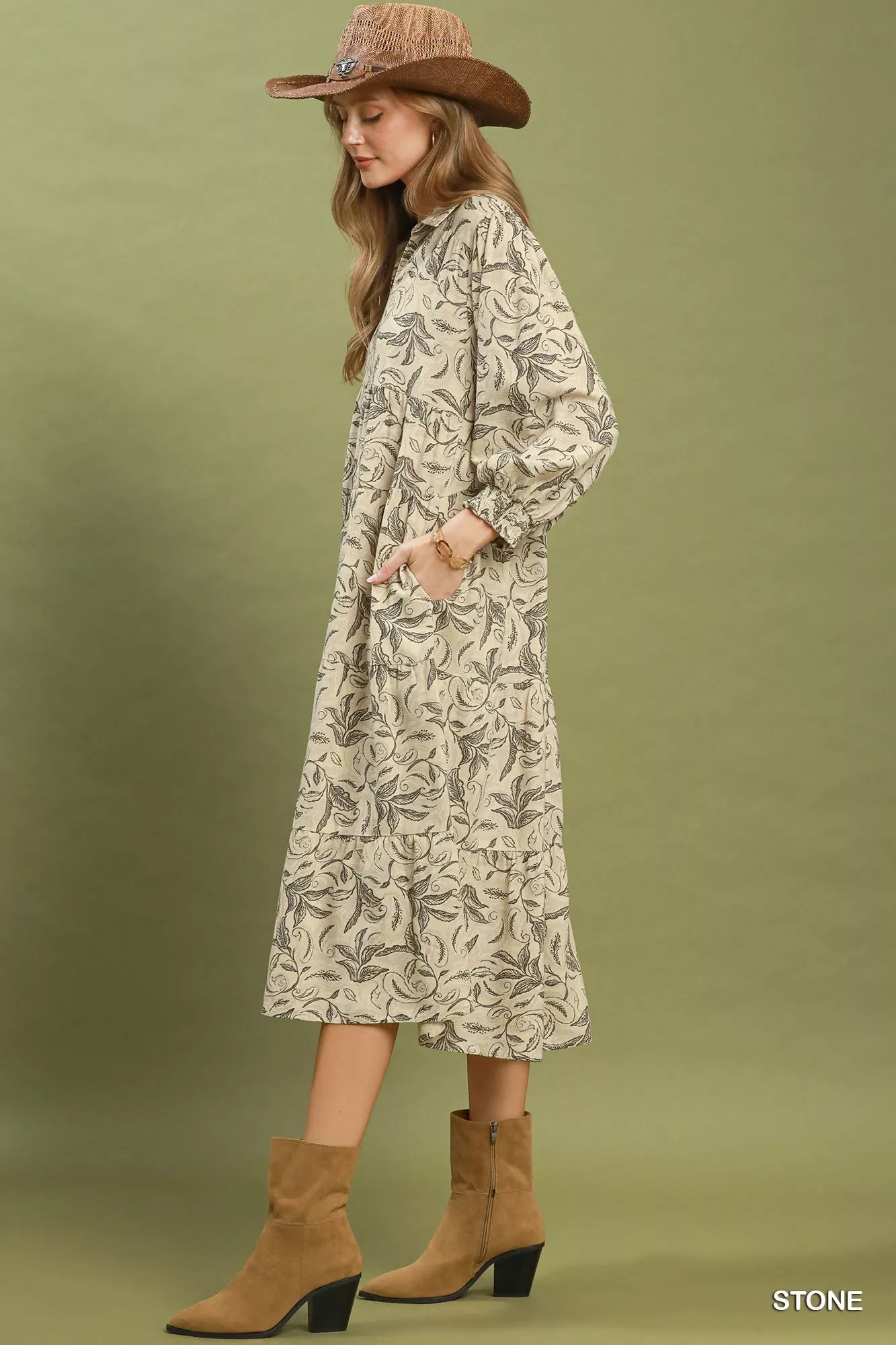Woman wearing a patterned dress and brown boots against a green background
