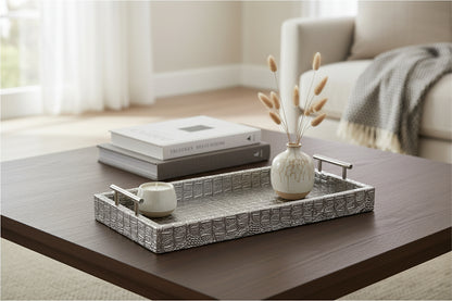 Silver faux alligator tray on a coffee table with decorative items on it.