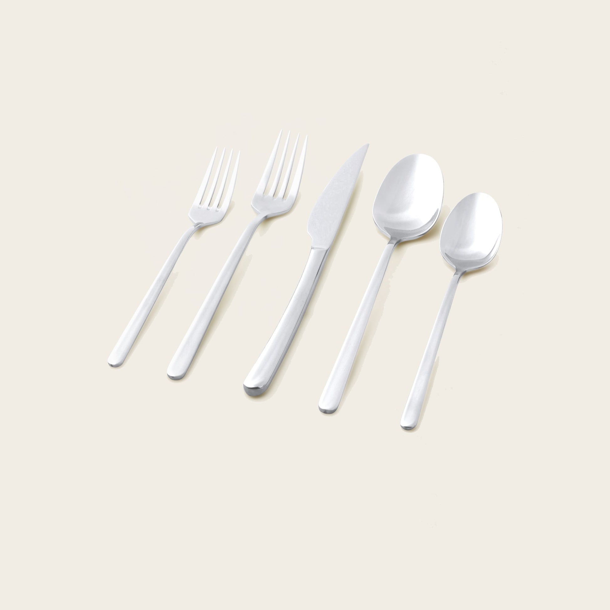 Set of silver cutlery including forks, a knife, and spoons on a beige background
