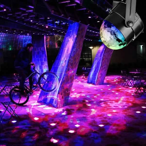 Colorful disco ball on a stand with a person on a bike in a vibrant indoor setting.