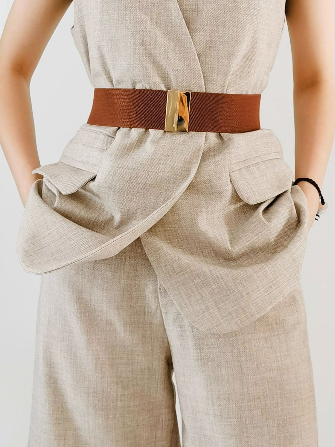 Beige jumpsuit with a brown belt on a plain background