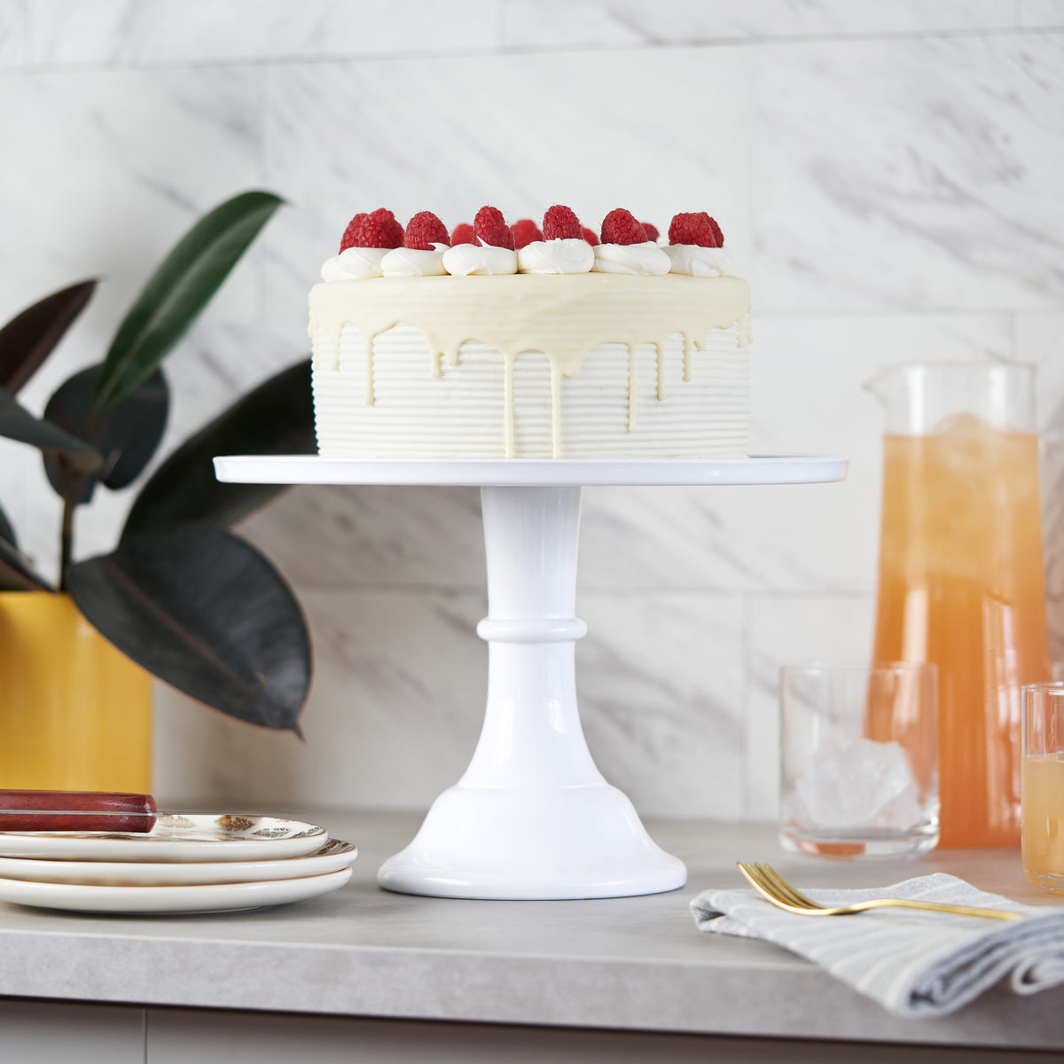 White melamine cake stand with a white cake with berries sitting on a buffet table.