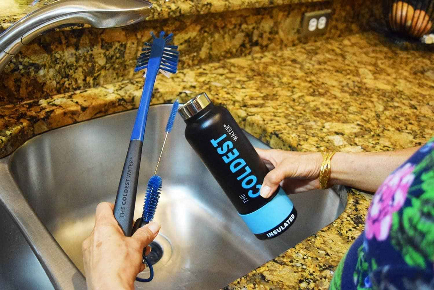 Person cleaning a water bottle with a brush in a kitchen sink.