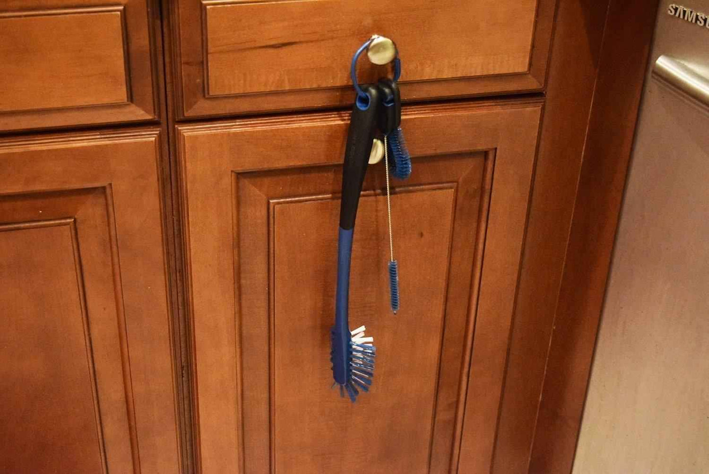 Blue brush and scrubber hanging on a wooden cabinet door