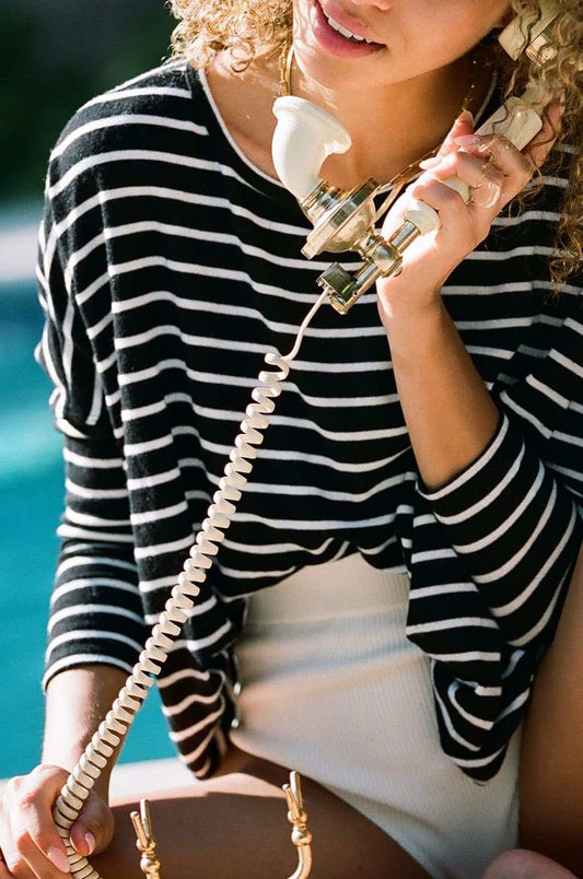 Person in a striped shirt holding a vintage phone with a blurred background