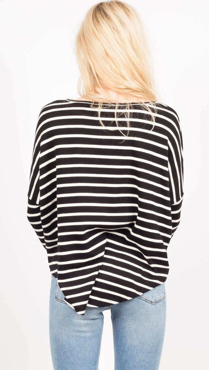 A woman viewed from behind wearing a black and white horizontally striped long-sleeve top and light blue jeans against a plain white background.